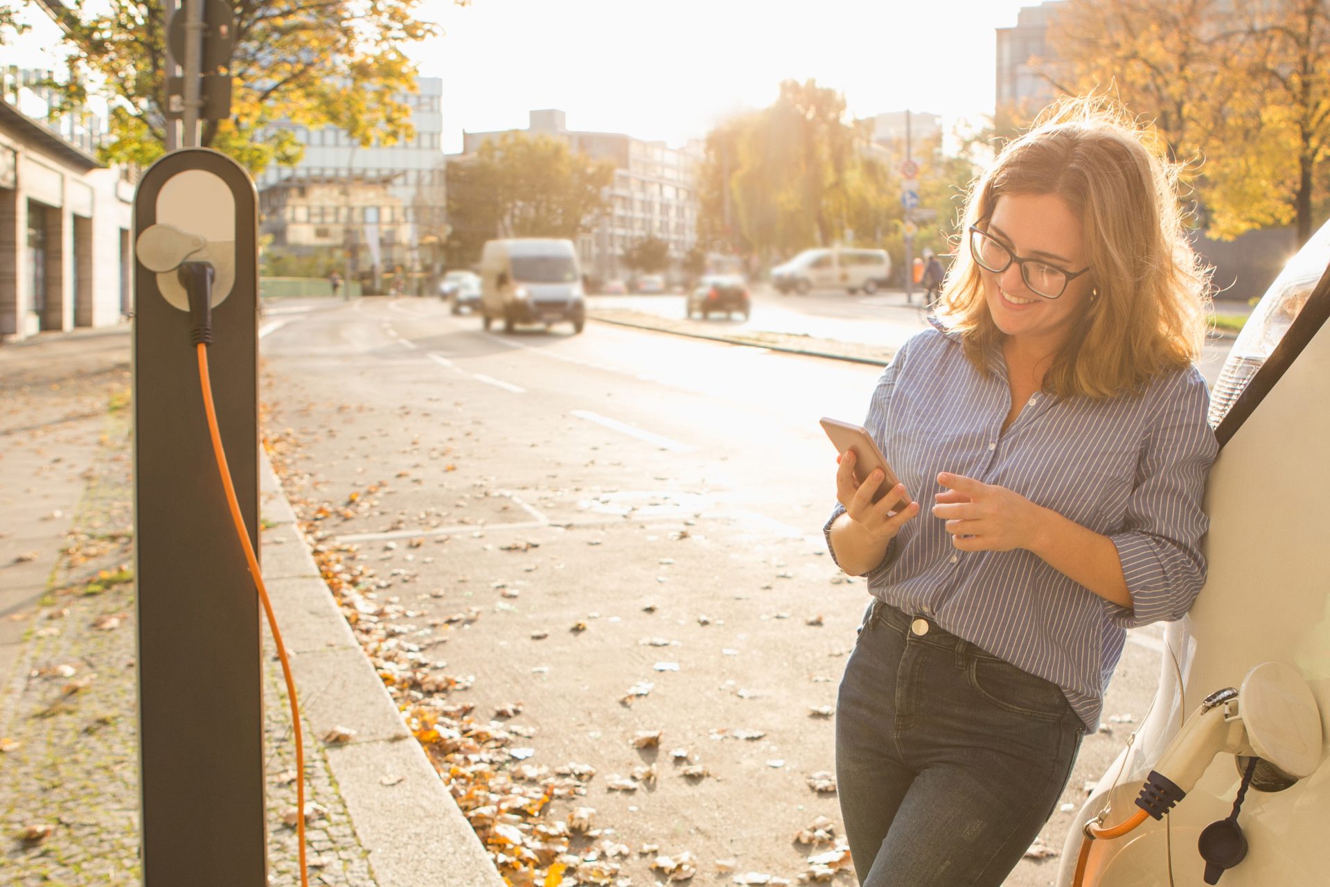 Frau schaut aufs Handy, während ein Elektroauto geladen wird, Semke Elektrotechnik